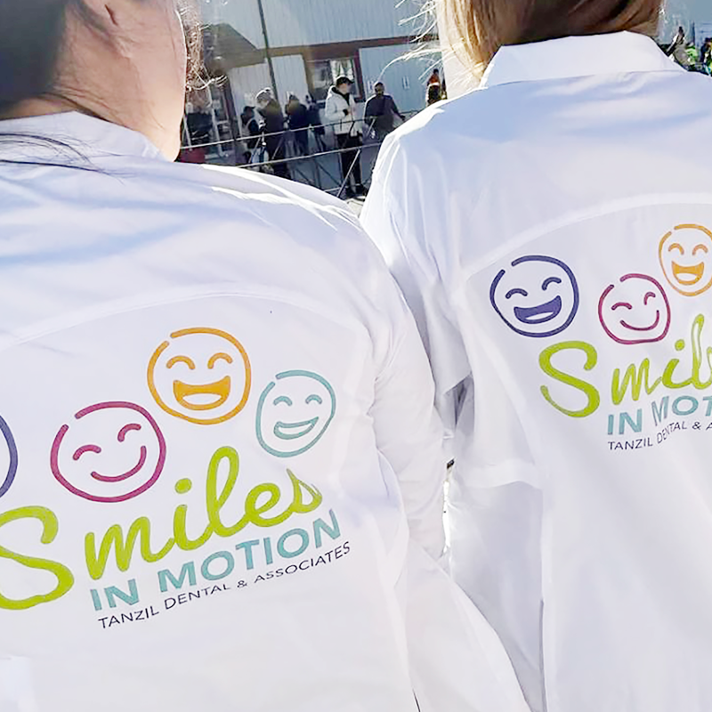 PTC_25_WebPortfolio_TZ_Jacket Two women wearing white jackets with smiley faces and the words Smiles in Motion, Tanzil Dental & Associates on the back.